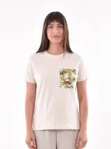 Remera color crudo de corte recto, con cuello redondo y bolsillo en el pecho con estampado camuflado en tonos verdes y marrones.