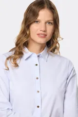 Camisa blanca de corte clásico, cuello camisero y mangas largas con puños abotonados. Cierre frontal con botones color madera.