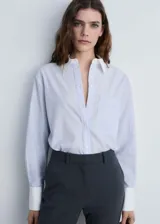 Camisa celeste a rayas verticales, de corte recto y manga larga con puños abotonados en blanco. Presenta cuello camisero blanco, cierre frontal con botones y un bolsillo de parche en el pecho.