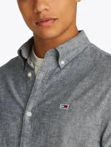 Camisa de manga larga Tommy Jeans, confeccionada en algodón y lino color gris jaspeado. Tiene cuello abotonado, cierre con botones, corte regular y logo bordado en el pecho.