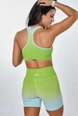 Conjunto deportivo de top y short con degradé de verde lima a celeste. El top es de espalda deportiva con logo "bk." en el frente. El short es tiro alto.