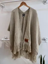 Ruana color arena confeccionada en telar artesanal con lana merino uruguaya 100% pura sin teñir, con flecos en el borde inferior.