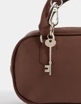 Cartera bowling color marrón chocolate, de cuero sintético, con doble asa corta, correa larga regulable y desmontable, y charm colgante.