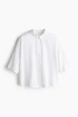 Camisa blanca de lino y viscosa, de corte holgado, con cuello clásico, botones frontales, mangas cortas y bajo redondeado.