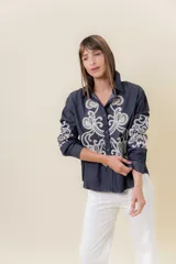 Camisa de denim liviano color azul oscuro con bordado artesanal en tono crudo en el frente y en las mangas. Presenta cuello clásico y cierre frontal con botones, con un calce relajado.
