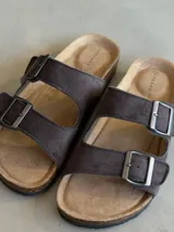 Sandalias de cuero sintético color marrón con doble tira y hebillas metálicas ajustables.