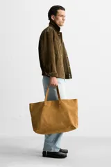 Bolso tipo shopper color marrón claro, fabricado en piel con acabado serraje. Tiene un compartimento principal con cierre imantado y un bolsillo interior con cremallera. Cuenta con dos asas de mano fabricadas en piel.