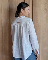 Camisa a rayas verticales color beige y blanco, de corte holgado, con cuello con volados, cierre parcial con botones y mangas largas con puños abotonados.