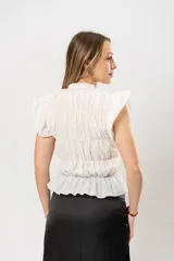 Top blanco con textura arrugada, cuello redondo, sin mangas y volados en los hombros.