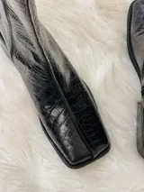 Bota negra de caña media con textura de cocodrilo, punta cuadrada y tacón bajo.