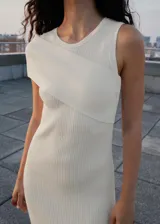 Vestido largo de punto acanalado color blanco roto, con cuello redondo y diseño entallado. Presenta un detalle asimétrico en el hombro derecho.