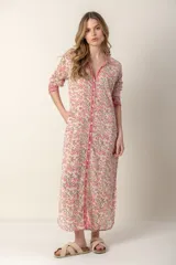 Vestido largo con estampado floral en tonos rosa y verde sobre fondo blanco. Tiene cuello con volantes, cierre frontal con botones y mangas largas con puños elásticos.