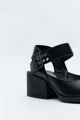 Zapato negro tipo zueco con acabado charol, tira ancha con hebilla metálica y taco ancho de altura media.
