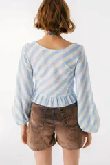 Blusa blanca de lino con escote en V, mangas largas abullonadas y frunce central.