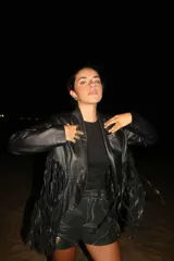 Chaqueta de cuero negra con solapas, cierre frontal con broche y flecos en mangas y ruedo.
