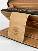 Billetera grande de cuero tricolor: negro, blanco con textura de cocodrilo y marrón claro. Tiene cierre de cremallera, correa de mano y botón de cierre con logo de búho.