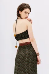 Top crop estilo bandeau con escote fruncido y tirantes finos cruzados en la espalda. Confeccionado en tela estampada con diseño floral en tonos mostaza, verde y terracota sobre fondo negro.