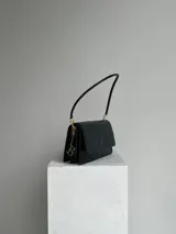 Cartera negra de hombro con textura tipo cocodrilo, doble compartimento interno, dije metálico con la letra B y cierre con broche imán.
