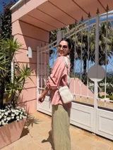 Bandolera pequeña tipo 'phone bag' de símil cuero color rosado pálido, con cierre de cremallera y correa ancha de tela con diseño de chevron en tonos claros.