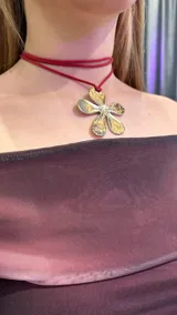 Gargantilla con cordón doble rojo y dije de flor plateada y dorada con un cristal en el centro.