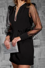 Vestido corto negro con escote en V, mangas largas abullonadas de tul con lunares blancos y lazo decorativo en la cintura.