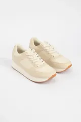 Zapatillas acordonadas color beige con suela blanca y detalles en marrón claro.