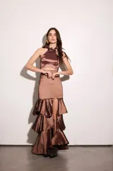 Falda larga color marrón con textura brillante, corte ajustado en la cintura y falda con volados en capas y tajo lateral.
