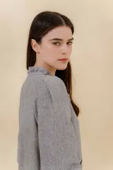 Blusa color beige con cuello mao con volantes, manga larga con puño elástico y cierre frontal con botones ocultos.