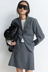 Blazer gris de corte entallado, con solapas de muesca, botonadura sencilla, bolsillo superior insertado y bolsillos delanteros. Tiene hombreras, botón decorativo en los puños y abertura atrás.