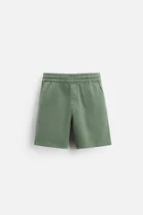Bermuda color verde militar de corte relajado, confeccionada en tejido de algodón. Tiene cintura elástica ajustable con cordón interior, bolsillos frontales y bolsillo trasero de parche.