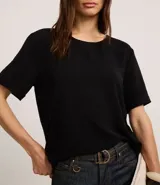 Blusa blanca de poliéster con cuello redondo, mangas cortas, cierre trasero en forma de gota, pequeñas aberturas laterales y acabados en pespuntes en las mangas y el cuello.