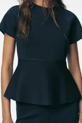 Top azul marino de punto con cuello redondo y manga corta. Tiene corte a la cintura y peplum en el bajo.