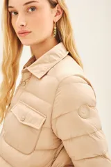 Campera puffer color beige con cuello camisero, cierre con botones a presión, bolsillos con solapa en el pecho y relleno de plumas.