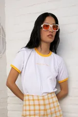 Remera blanca de algodón con ribete amarillo en cuello y mangas, y frase bordada en color naranja.