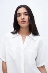Blusa verde con escote en V, cuello camisero, manga corta y dos bolsillos en el pecho.