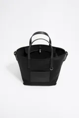Bolso shopper mediano Bimba y Lola color negro, con doble asa de mano y correa bandolera ajustable y extraíble. Presenta un parche rectangular con el logo de la marca en la parte frontal.