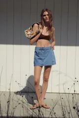 Minifalda pantalón de tiro alto confeccionada en denim celeste, con bolsillos delanteros y traseros. Presenta cierre frontal cruzado con cremallera oculta y botón metálico.