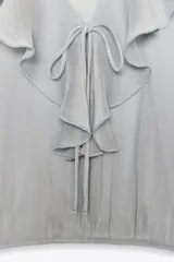Blusa color marrón con escote en pico, manga larga abullonada con elástico en los puños y volantes en el escote y mangas.