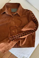 Camisa marrón de gamuza con cuello clásico, cierre con botones a presión y mangas largas con detalles artesanales calados.