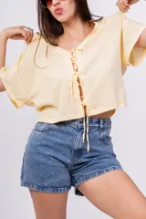 Remera color amarillo pálido de corte holgado, escote en V con lazo y mangas cortas.