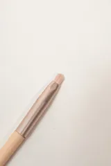 Brocha de maquillaje con mango en tono nude y cabezal metálico.