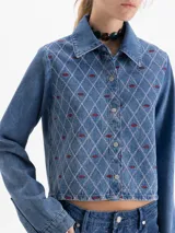 Camisa de denim azul de manga larga, corte cuadrado y silueta corta. Presenta un bordado integral en patrón de rombos con detalles en rosa y bordeaux.