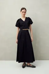 Falda midi blanca con pequeños lunares negros, de corte acampanado y cintura alta con pliegues.