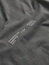 Camiseta gris oscuro de manga corta y cuello redondo, con calce holgado y parche rectangular con diseño abstracto en el pecho.