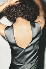 Vestido midi de satén color gris oscuro, con escote asimétrico, manga sisa, detalle de aplique dorado en el hombro y frunces laterales.