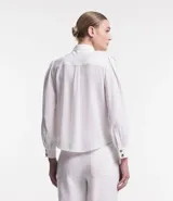 Camisa blanca de crepé con cuello solapa, abotonada, mangas largas abullonadas y sin estampado.