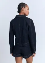 Chaqueta corta de denim azul oscuro, con cuello de solapa, dos bolsillos de parche en el pecho y cierre frontal de botones. Presenta costuras contrastantes y puños abotonados.