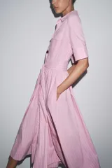 Vestido camisero midi de popelina a rayas verticales rosas y blancas, con cuello solapa, manga corta, bolsillos de parche en el pecho, cinturón de lazo ajustable y cierre frontal con botones.