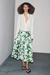 Falda midi de tiro medio con estampado floral en tonos blanco y celeste sobre fondo verde. Presenta detalle de tablas y cierre lateral con cremallera oculta.