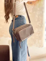 Bandolera color visón, fabricada en cuero con forro de tela. Tiene bolsillo interior y exterior. Entra billetera grande.